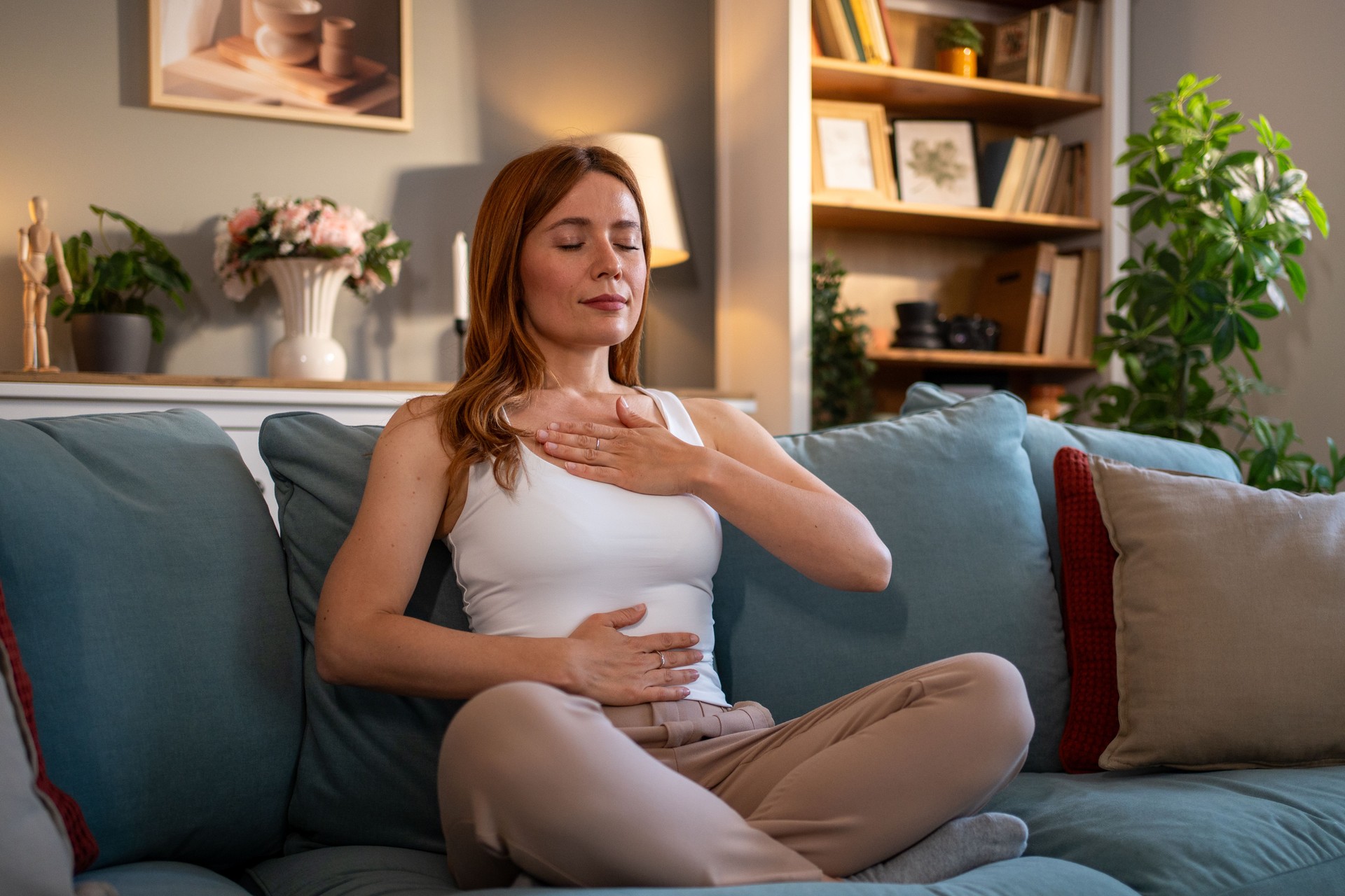 Serene woman practicing diaphragmatic breathing on sofa at home