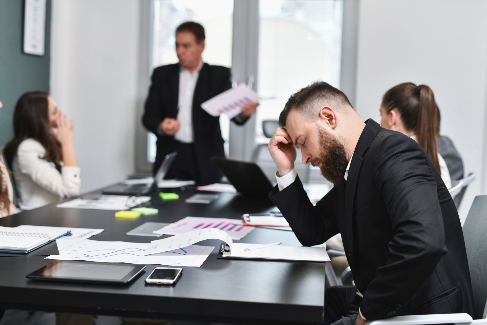 Male Businessman Feeling Stressed and Tired in Business Meeting Sitting With Closed Eyes